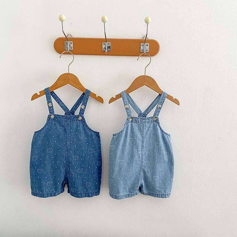 White Dots Denim Overalls hanging on wooden hangers with a polka dot pattern.