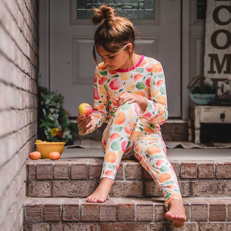 Baby pajamas with a colorful citrus fruit print on a soft pink background, long sleeves and pants.