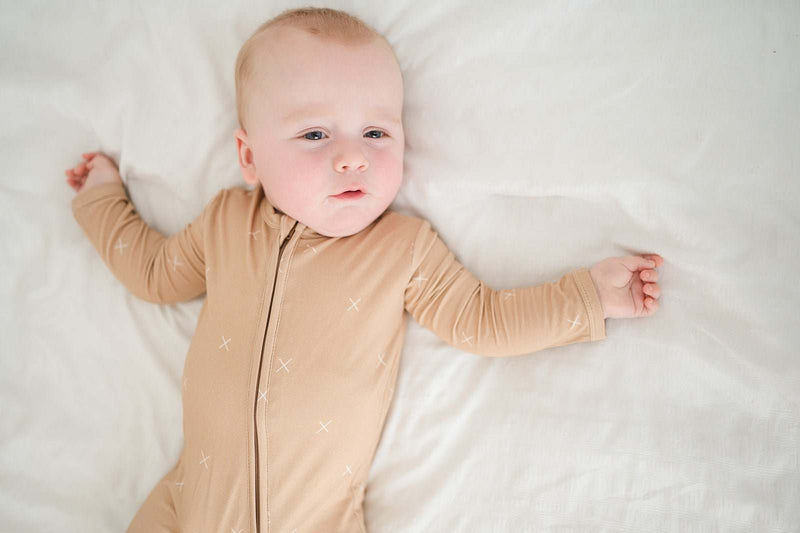Baby wearing beige zipper romper with X print, featuring a two-way zipper and fold-over cuffs, made from soft bamboo viscose.