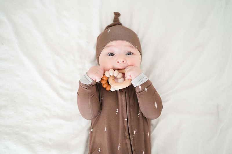 Baby wearing brown lightning zipper romper with fold-over cuffs and 2-way zipper lying on a soft surface.