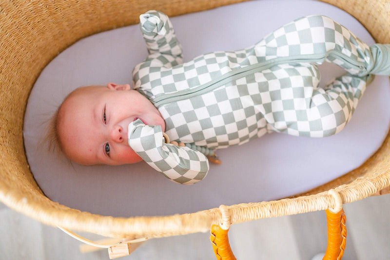 Baby wearing jade checker zipper romper with fold-over cuffs in a basket.