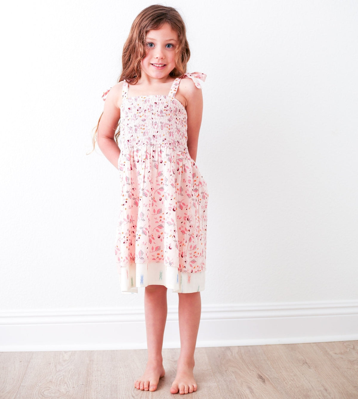 Pink floral baby dress with smocked top, adjustable tie straps, and a layered skirt
